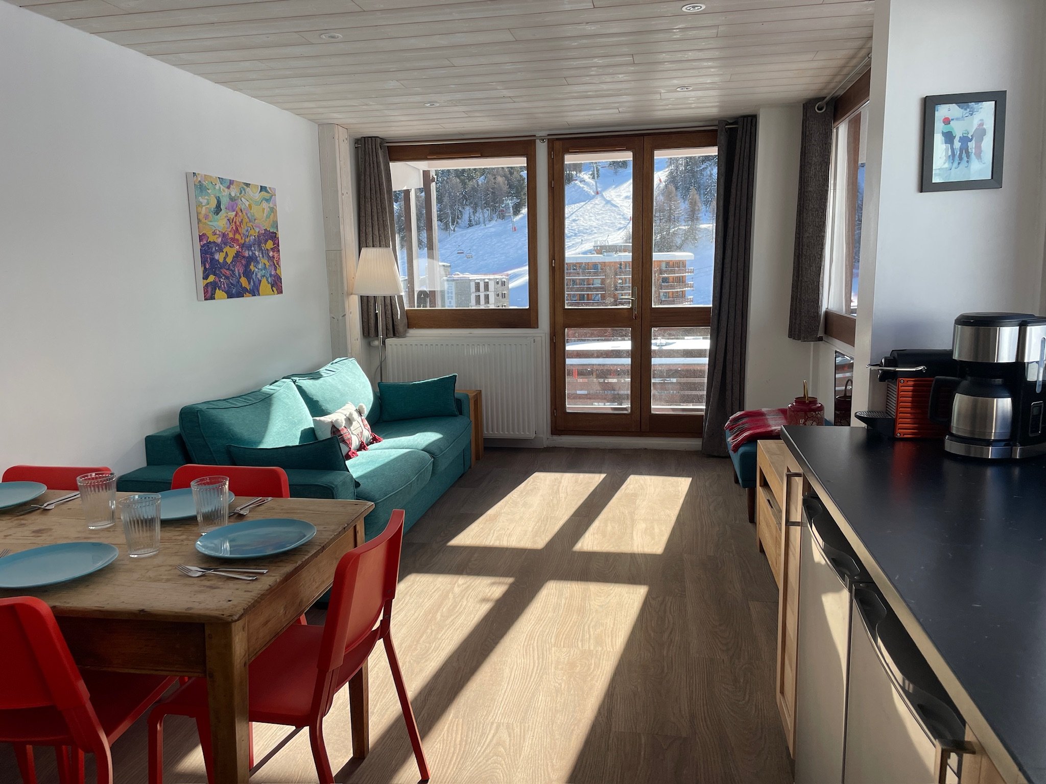 Open-plan living space at SnowBadgers with dining table, sofa, and balcony doors onto the snow